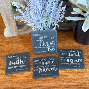 May include: Four square slate coasters with white lettering featuring Bible verses. The coasters include the phrases "For we walk by faith, not by sight", "I can do all things through Christ", "Jesus Christ is the same yesterday and today and forever", and "This is the day the Lord has made".