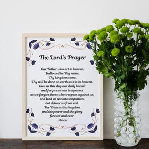 May include: A framed print of The Lord's Prayer with a decorative floral border. The print is on white paper with black text. The frame is light brown wood.