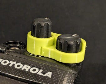 Könnte beinhalten: Eine 3D-gedruckte Knopf-Abdeckung in Limettengrün mit zwei schwarzen Knöpfen. Die Abdeckung ist so konzipiert, dass sie über die Knöpfe eines Motorola-Radios passt.