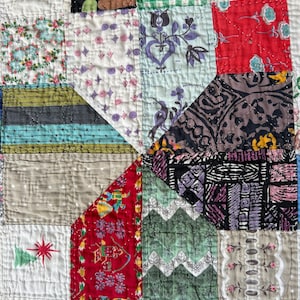 May include: A handmade patchwork quilt featuring a variety of fabric squares with diverse patterns including green gingham, red floral, black and white geometric, and white fabric with small embroidered red stars and green pine tree motifs.