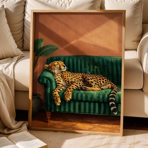 May include: A framed art print depicts a cheetah resting on a green striped sofa. The cheetah has a spotted coat and is lying down with its eyes closed. The background features a terracotta wall and a potted plant.