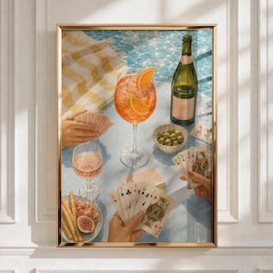 May include: A framed wall art print depicting a summer scene with a glass of orange spritz, a green wine bottle, a small bowl of green olives, a plate of breadsticks and figs, and hands holding playing cards over a light blue tiled surface.