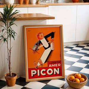 May include: Framed vintage advertisement poster for Picon Aperitif. The poster features a cartoon figure in a suit carrying bottles, set against an orange background. The poster is in a wooden frame and is leaning against a wall next to a potted plant and a basket of oranges.