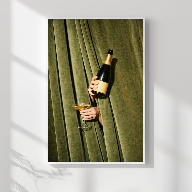May include: A dark glass bottle with a tan label and a clear stemmed glass filled with a golden liquid, both held against a backdrop of heavy, vertically pleated olive green velvet fabric that creates deep shadows and highlights.