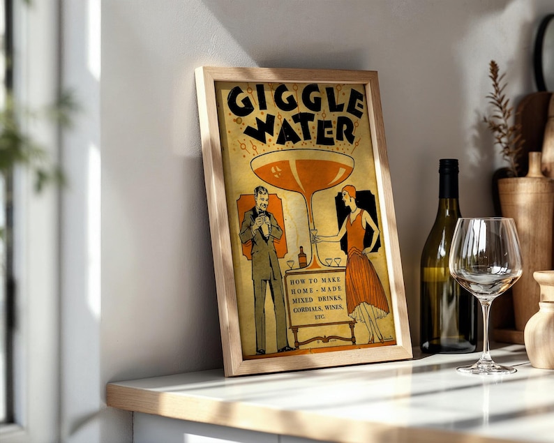 Op de afbeelding: Een ingelijste vintage print met de woorden "GIGGLE WATER". Het kunstwerk toont een groot cocktailglas en figuren in historische kleding. De print bevat ook tekst over het maken van mixdranken. Een fles en een wijnglas staan ernaast.