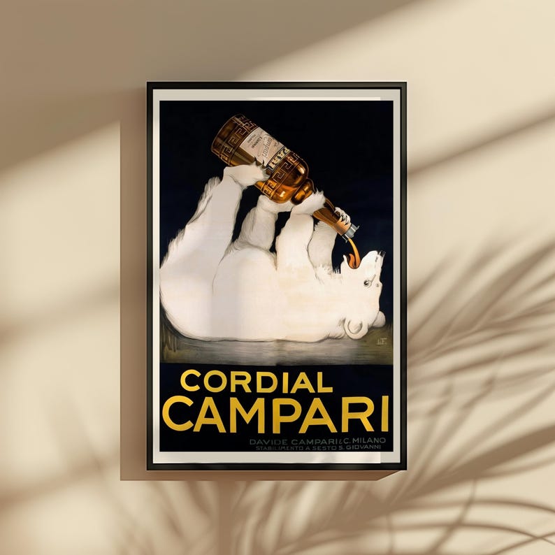 Pu&ograve; includere: Una pubblicit&agrave; vintage incorniciata per Cordial Campari. Il poster presenta un orso polare bianco reclinato che beve da una bottiglia. La bottiglia versa un liquido marrone nella bocca dell'orso. Il testo "Cordial Campari" &egrave; in lettere d'oro.