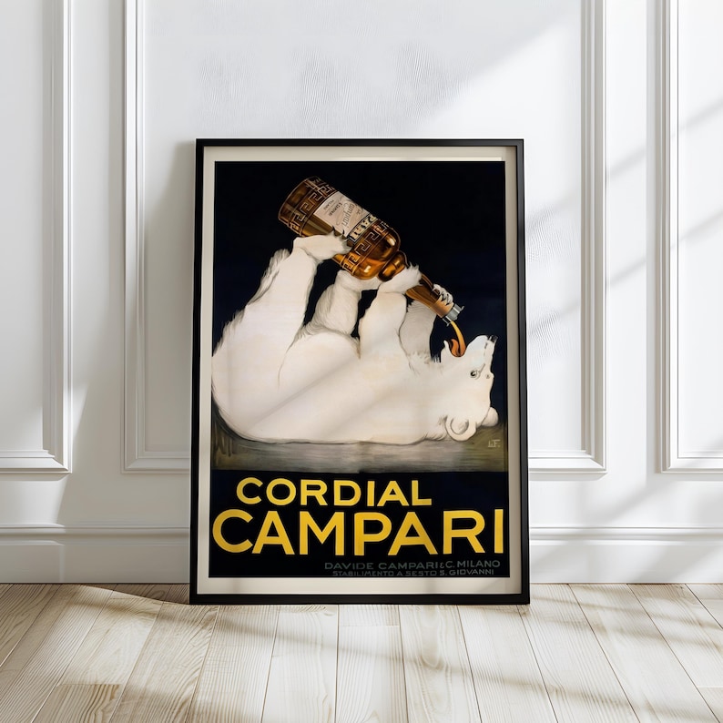 May include: Framed vintage advertisement poster for Cordial Campari. The poster features a white polar bear pouring a bottle of Campari into its mouth. The text "Cordial Campari" is in gold lettering on a black background.