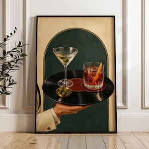 May include: A framed wall art print featuring a hand holding a black vinyl record as a serving tray. On the record sits a martini glass with olives, a small gold bowl of olives, and a rocks glass containing an amber cocktail with an orange peel.