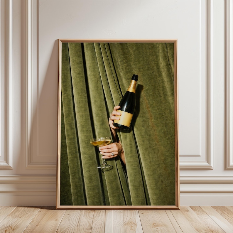 Moody champagne wall art featuring hands holding a champagne bottle and coupe through green velvet curtains, styled as vintage cocktail bar decor.