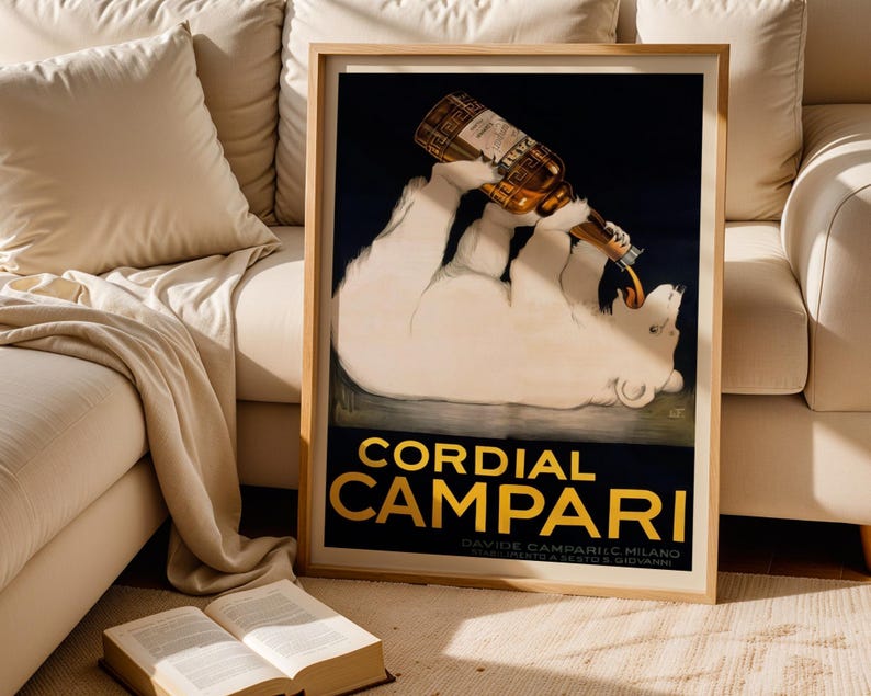 Pu&ograve; includere: Un poster vintage incorniciato per Cordial Campari. L'opera presenta un orso polare bianco che beve da una bottiglia di Campari. Il testo "CORDIAL CAMPARI" &egrave; in lettere dorate su sfondo nero. Il poster &egrave; in una cornice di legno.