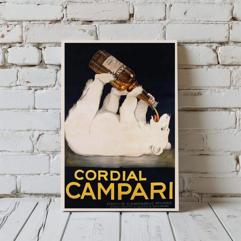 Pu&ograve; includere: Poster pubblicitario vintage con un orso polare che versa Campari da una bottiglia. La scritta "Cordial Campari" &egrave; gialla su sfondo scuro. Il poster incorniciato &egrave; appeso a un muro di mattoni bianchi.