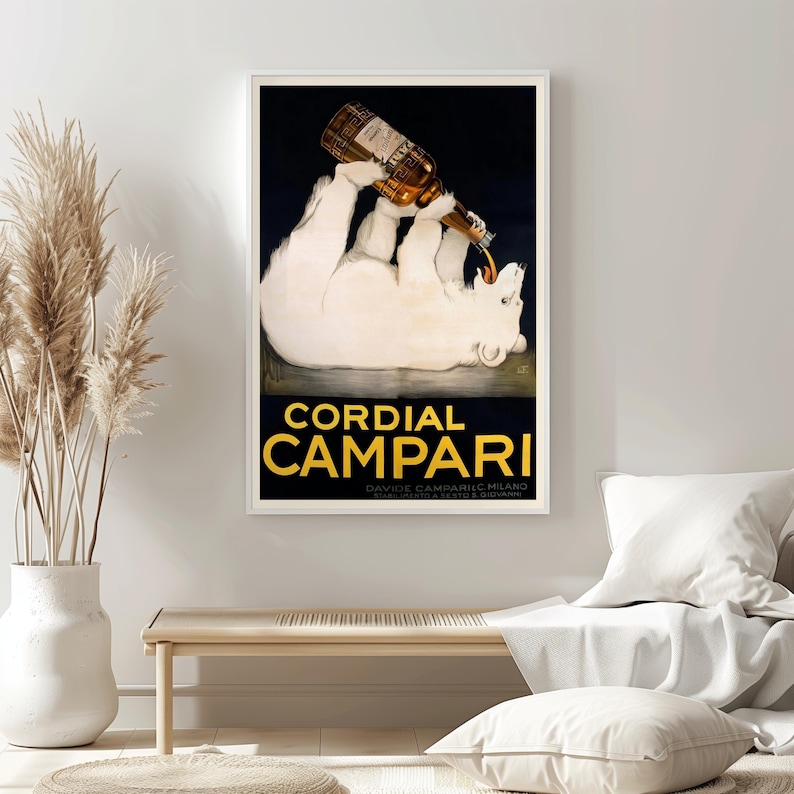 Pu&ograve; includere: Un poster vintage incorniciato per Cordial Campari. Raffigura un orso polare bianco che beve da una bottiglia. Il testo "CORDIAL CAMPARI" &egrave; in oro su sfondo blu scuro, un design classico.