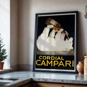 Pu&ograve; includere: Un poster vintage incorniciato che pubblicizza Cordial Campari. Raffigura un orso polare bianco che beve da una bottiglia di Campari. Il testo "Cordial Campari" &egrave; in lettere dorate su sfondo blu scuro.