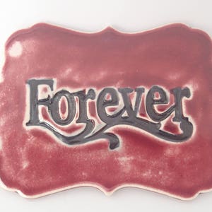 May include: A burgundy ceramic tile with a white border and the word "Forever" written in black script.