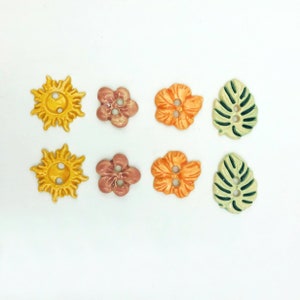May include: Set of eight ceramic buttons featuring various designs, including a sun, flowers, and leaves. The buttons are in shades of yellow, orange, pink, and green.