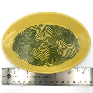 May include: A yellow oval dish with a green leaf pattern. The dish is approximately 6 inches long.