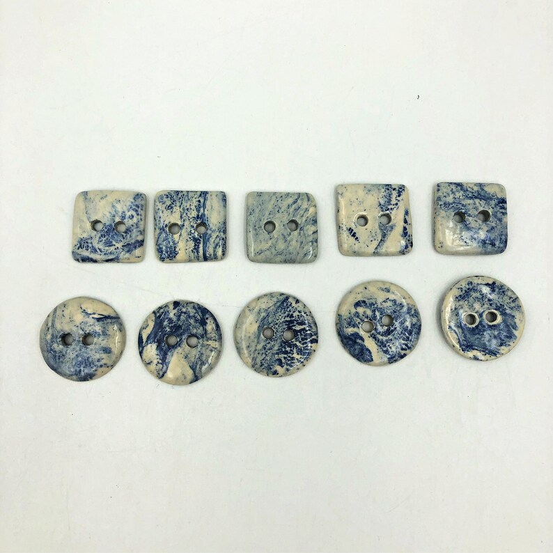 Pu&ograve; includere: Una collezione di dieci bottoni in ceramica, di forma quadrata e rotonda. I bottoni presentano un motivo marmorizzato blu e crema. Ogni bottone ha due fori per cucire.