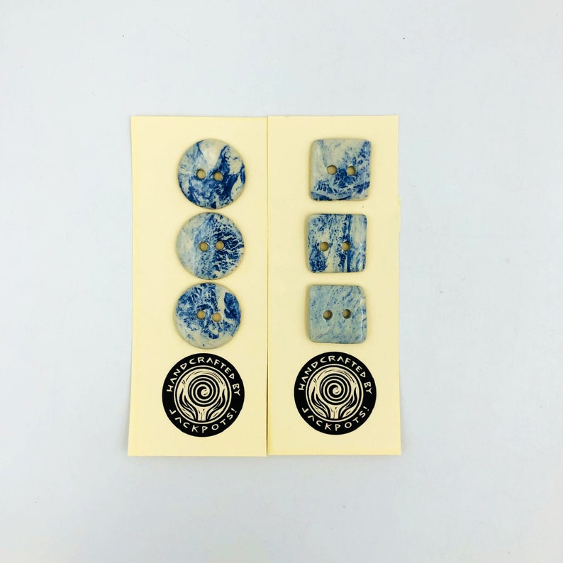 Pu&ograve; includere: Due set di bottoni, uno rotondo e uno quadrato, con un design blu e bianco marmorizzato. Ogni bottone ha due fori. I bottoni sono esposti su cartoncini color crema con un logo in bianco e nero che recita "HANDCRAFTED BY JACKPOTS!"
