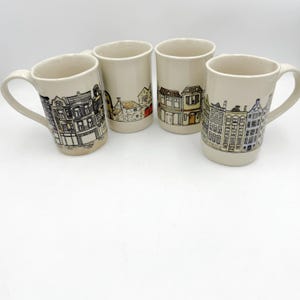 May include: Four ceramic mugs with a cream-colored base and a hand-drawn illustration of buildings. Each mug features a different building design in black, white, and shades of brown, yellow, and blue. The mugs have a curved handle.