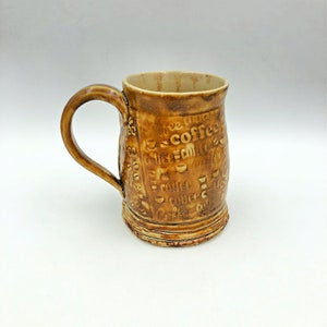 May include: A brown ceramic coffee mug with a handle. The mug is decorated with the word "coffee" repeated many times in a stylized font.