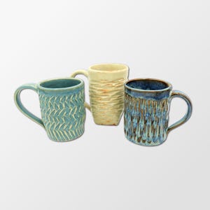May include: Three ceramic mugs with different textured patterns. The mugs are in shades of blue, white, and brown.
