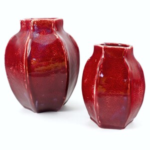 May include: Two red ceramic vases with a textured, swirling pattern. The larger vase is wider and shorter than the smaller vase.