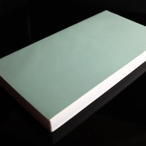 Può includere: Un blocco note rettangolare di colore verde chiaro con bordi bianchi.