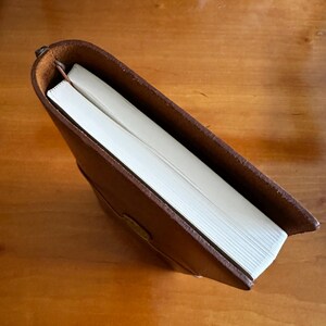 May include: A brown leather-bound journal with a white bookmark. The journal is closed and the spine is visible.