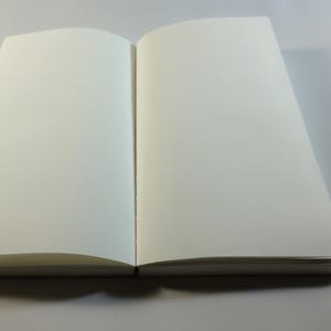 May include: A blank, white notebook with a hard cover and a spine. The notebook is open to a blank page.