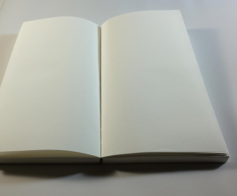 May include: A blank, white notebook with a hard cover and a spine. The notebook is open to a blank page.