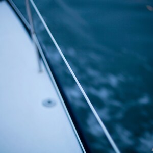 May include: A close-up of a white boat deck with a rope railing and a blue water background.