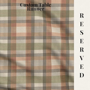 May include: A table runner featuring a plaid pattern in muted shades of peach, sage green, gray, and cream. The text Custom Table Runner is printed at the top, and the word RESERVED is printed vertically along the right side of the fabric.