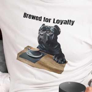 May include: White t-shirt with a graphic of a black dog and the words "Brewed for Loyalty". The dog is sitting at a table with a coffee cup. The design is printed on the front of the shirt.