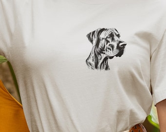 May include: A light beige t-shirt featuring a detailed black and white illustration of a dog's head in profile. The graphic is positioned on the upper left chest area of the shirt. The shirt has short sleeves and a crew neck.