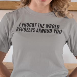 May include: Gray t-shirt with the text "I FROGOT THE WROLD REVOELVS ARNOUD YOU" printed on the front.