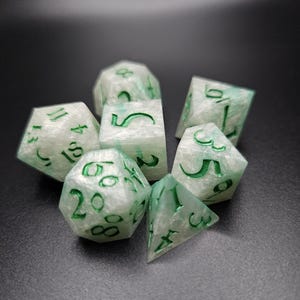 Puede incluir: Un conjunto de siete dados blancos con números verdes. Los dados están hechos de un material translúcido, y los números son visibles a través del material.