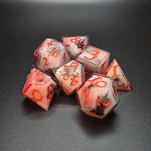 Puede incluir: Juego de siete dados poliédricos con temática de Halloween. Los dados son blancos con números y detalles rojos, incluyendo telarañas y arañas. Diseñados para juegos de rol de mesa.