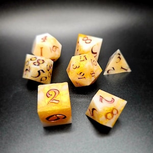 Puede incluir: Conjunto de seis dados blancos y dorados con números rojos. Los dados están hechos de un material translúcido con un acabado brillante.