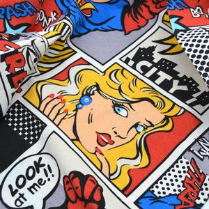 May include: Comic book-style fabric featuring panels with bold colors and pop art illustrations. The design includes a blonde woman, speech bubbles, and action words like "THRASH" and "CITY". The overall theme is a vibrant, retro comic book aesthetic.