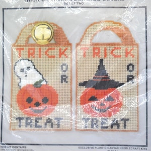 May include: A set of two plastic canvas needlecraft kits for Trick or Treat door covers. The designs feature orange pumpkins, a white ghost, and a black witch hat, with the text Trick or Treat stitched in black and orange on a tan background.