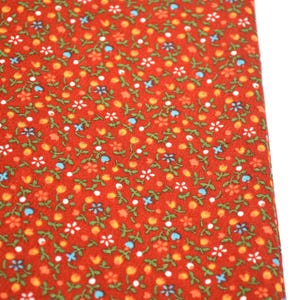 May include: A vibrant red fabric featuring a dense, repeating pattern of tiny white, blue, and orange flowers interspersed with small green leaves and stems. The textile displays a consistent, intricate floral print across the entire surface.