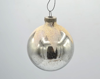 May include: A silver Christmas ornament with a frosted, light-colored top. The round ornament has a reflective surface and is suspended by a thin wire. The ornament is a classic holiday decoration.