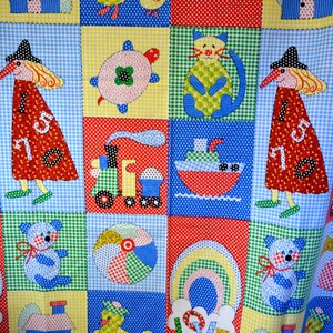 May include: A colorful patchwork fabric featuring squares with various appliqued designs. The designs include a witch, a cat, a turtle, a teddy bear, a ship, a train, a beach ball, and a rainbow. The fabric is a mix of polka dots and gingham patterns.