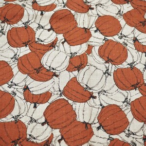 May include: A fabric textile featuring a repeating pattern of pumpkins in burnt orange and off-white. Each pumpkin is outlined in thin black lines, creating a dense, overlapping design across the entire surface of the material.