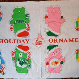 May include: A white fabric panel featuring printed Care Bears holiday ornaments. The design includes multiple colorful bears in festive attire, candy canes, and gifts, with the red text HOLIDAY CARE BEARS ORNAMENTS printed in the center.