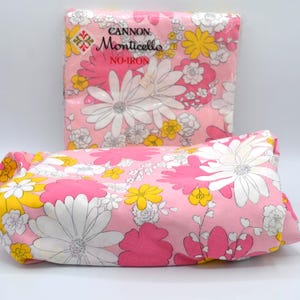 May include: Pink floral bedsheets with large white, yellow, and pink flowers. The sheets are packaged and folded, with the brand name "Cannon Monticello" visible. The design features a repeating pattern of daisies and other floral elements.