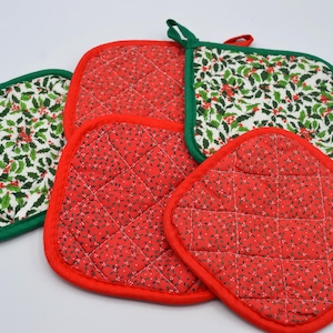 May include: A set of four square quilted pot holders featuring two distinct patterns. Two pot holders display a white background with a green holly leaf and red berry print and green trim, while two feature a red background with small white floral patterns.