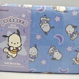 May include: A Sanrio Pochacco Home Collection full sheet set in plastic packaging. The set includes a flat sheet, a fitted sheet, and two standard pillowcases. The fabric is blue with a repeating pattern of white Pochacco characters, purple crescent moons, and white stars.
