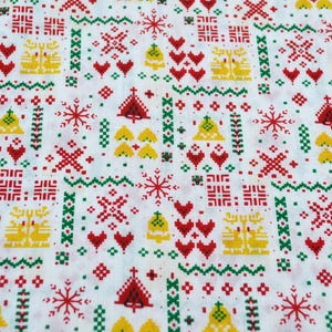 May include: White fabric with a repeating pattern of red, yellow, and green Christmas-themed pixelated designs. The pattern includes Christmas trees, bells, snowflakes, and hearts.