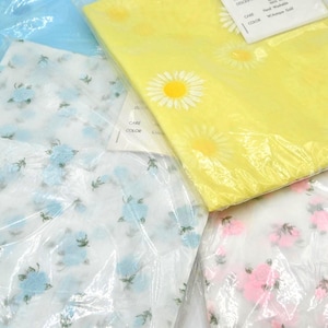 May include: Several fabric pieces in plastic packaging. One is light blue, another is yellow with white daisies, and two others are white with blue and pink floral patterns. The fabrics appear to be lightweight and possibly for sewing or crafting.